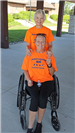 One women in an orange shirt in a wheelchair and a women standing behind her in an orange shirt.